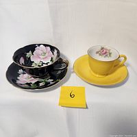 Photo showing both teacup and saucer sets side by side on a white cloth background, displaying their designs and colors as described by seller.
