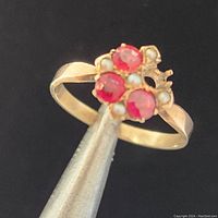 Close-up front view of vintage 10k gold ring with three pinkish-red stones and four seed pearls, one stone missing.