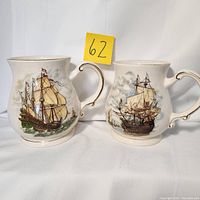Pair of large Sadler beer steins with old galleon sailing ship painted designs in cream glaze and gold trim, showing full side profiles and handles.