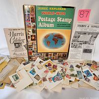 Photo of Harris Explorer stamp album, Harris 1975-76 catalog, Littleton 1976 catalog, and visible loose stamp envelopes