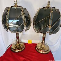 Pair of vintage tri-light touch lamps with brass tone bases and smokey gray glass panels displaying frosted and etched designs arranged around glass clips. One lamp has a broken glass clip visible on a panel.