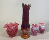 Photo of the four vases showing an 11 inch multicolored Indiana Heirloom Sunset vase with ruffled edge, one deep cranberry Fenton hobnail glass vase, and two smaller hobnail cranberry glass vases.