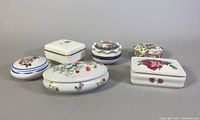 All six vintage porcelain trinket boxes in varied shapes and floral decorations arranged together.