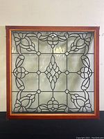 Full view of antique leaded glass window in wooden frame against white wall.