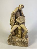 Full view of the hand carved sculpture showing the seated man playing accordion and detailed cloak and base.