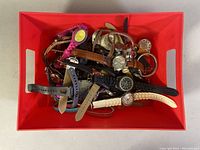 Overhead photo showing a large box filled with assorted watches of various styles and colors, including metal, leather, silicone, and plastic bands.