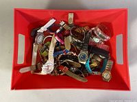 Top view showing a red bin filled with over 20 various wristwatches with different band materials and colors.