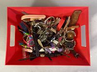 Wide view of a red tray filled with a large assortment of wristwatches of varying styles and colors, showing diversity of the lot.