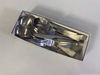 Box set showing stacked flatware utensils including spoons and forks in a tray.