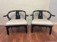 Front view of both black lacquer armchairs showing their shape, brass accents, and upholstery condition