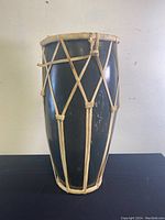 Side view of the bongo drum showing the dark wooden body with tan ropes laced around it