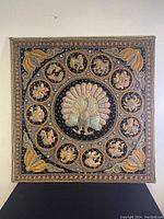 Full view of the vintage square wall hanging tapestry showing the central peacock and surrounding animal motifs in relief embroidery.