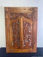 Front view of the closed carved wooden cabinet doors set within the decorative frame showing floral and leaf carvings.