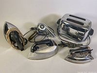 Photo showing all six vintage electric appliances: three irons, one toaster, one blow dryer, with cords wrapped.
