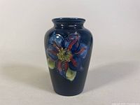 Front view of the Moorcroft bud vase showing the dark blue background and hand-painted flower with blue and red petals.