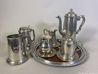 Photo shows a 14-inch pewter serving tray with a wood inset holding a coffee pot, stein, creamer, sugar bowl, and tankard with crest, highlighting the material and condition.