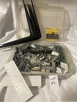 Photo showing the full plastic container with over 50 metal brackets, corner braces, including six medium black L-shaped brackets and various white and silver metal braces, some packaged.