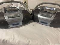 Two portable stereo CD player and radio systems placed side by side with remotes on top, showing general condition and overall appearance.
