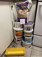 Overall stacked view of various concrete supply buckets and large bag with a small yellow plastic mixing tray in front and metal mixer stand visible