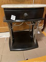 Front view of black end table showing drawer with metal knob, solid base and marble top