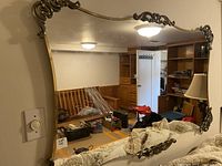 Front angled view of large wall mirror showing metal detailed edges, reflective surface, and general condition.