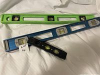 Three spirit levels: green 24-inch, blue 24-inch, and small black torpedo level on white fabric background.