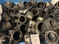 Box filled with assorted black PVC plumbing fittings including couplings and connectors with some threaded ends.