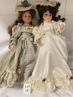 Front view of two porcelain collector dolls dressed in vintage style gowns showing detailed lace, floral decorations, and facial features