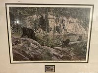 Framed artwork showing three black bears in a natural rocky lakeside forest setting with framed borders.