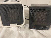 Both Honeywell small indoor space heaters, one white ceramic model and one black with knob control, placed side by side showing front and top handle.