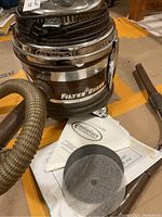 Photo of Filter Queen vacuum cleaner unit with hose, placed on floor next to extra filters including black mesh and white fabric types.