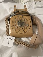 Front view of the beige rotary phone with handset resting beside it, rotary dial visible with letters and numbers.