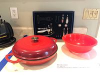 Full view of lot items: red cast iron skillet with lid, red Pyrex bowl, and Brookstone wine opener set with multiple accessories in black case.