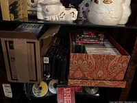 Box and open cases with DVDs and game discs showing assorted contents including music DVDs and video games.