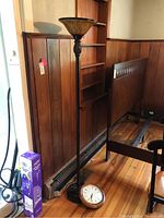 Full view of wood floor lamp standing next to Seiko wall clock placed on the floor.