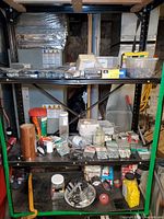Photo showing metal shelving unit with hardware packages including screws, bolts, nails, washers, plastic anchors and a copper roll, in basement environment.