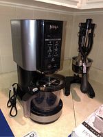 Ninja NC301 Ice Cream Maker and black manual citrus juicer side by side on kitchen counter.