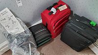 Mighty Max stair dolly in plastic wrap along with three rolling suitcases: red, black, and black with green accents