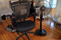 Front view of the black mesh office chair with armrests and the Amazon Basics floor fan beside it.