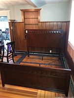 Full view of assembled queen bed frame showing headboard, footboard, and sideboards in a wood-paneled room.