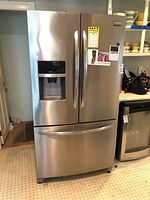 Front view of stainless steel French door refrigerator showing dual doors and bottom freezer drawer with integrated water and ice dispenser