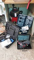 Photo showing Shop Vac wet/dry vacuum behind opened tool cases containing Kreg Jig components, RotoZip power tool in a black case, and Bosch router guide in a blue case.