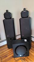 Two floorstanding speakers with height modules and powered subwoofer on hardwood floor