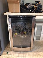 Front view of GE Profile wine cooler fridge showing stainless steel curved glass door and internal metal wine racks with some bottles inside.