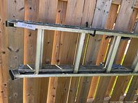 20-foot metal extension ladder hung on wooden fence, showing front side and hooks for extension.