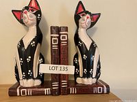 Pair of black and white cat bookends with red inner ear detail, depicted sitting on book-shaped bases painted dark brown with white and red spine markings.