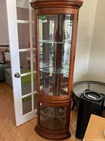 Full view of wooden curio cabinet showing curved glass front and top installed shelves