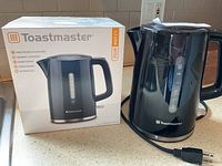 Photo showing black Toastmaster electric kettle beside its original box with brand and product information visible.