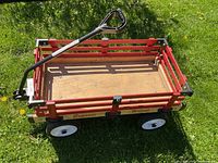 Side angle showing the red wooden sides, flat wooden base, and black pull handle extended forward on green grass.
