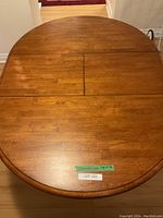 Round wooden kitchen table with an extension leaf inserted in the middle section and visible wood grain.